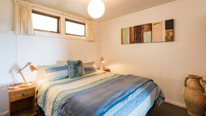 A bedroom with a bed, nightstands, a lamp, a vase, and artwork on the wall. - Allure Lodge cabin (Paihia)