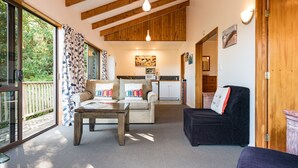 A spacious living area with a sofa, a coffee table, and a dark armchair. A kitchen is visible in the background with a microwave and cabinets. - Allure Lodge cabin (Paihia)