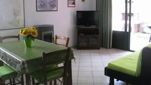 Un coin repas avec une table dressée pour deux personnes, un téléviseur posé sur un meuble et un canapé en arrière-plan.