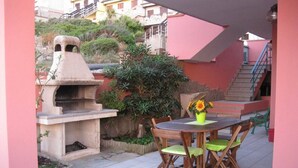 Une terrasse extérieure équipée d’un barbecue, d’une table avec des chaises et d’un escalier menant à un niveau supérieur.