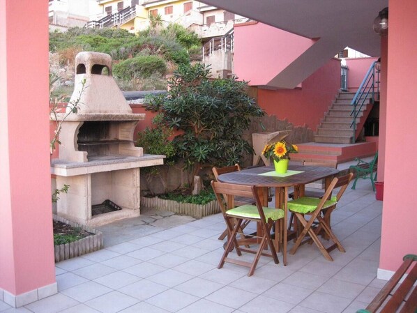 Une terrasse extérieure équipée d’un barbecue, d’une table avec des chaises et d’un escalier menant à un niveau supérieur.