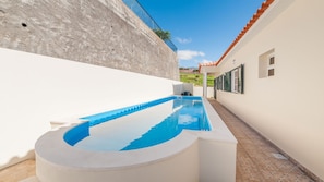 A swimming pool with a curved edge, surrounded by white walls and a tiled patio area. - Casa Eleanor by LovelyStay (Estreito da Calheta)