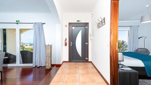 A hotel room with a bed, a desk, a chair, a view of the outdoors, and a door with a fire extinguisher. - Casa Eleanor by LovelyStay (Estreito da Calheta)
