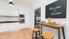 Une cuisine moderne avec des armoires blanches, un four encastré et un tableau noir sur lequel est écrit : « Bienvenue chez Eleanor ».