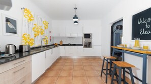 A modern kitchen with white cabinets, a black countertop, and a tiled floor. - Casa Eleanor by LovelyStay (Estreito da Calheta)