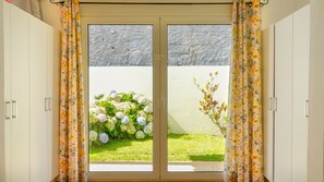 Una habitación con puerta corrediza de vidrio que da a un jardín con flores blancas y un árbol pequeño.