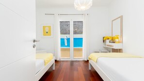 A hotel room with two beds, a bathroom, a view of a pool, and a mirror on the wall. - Casa Eleanor by LovelyStay (Estreito da Calheta)