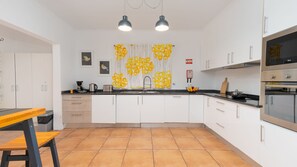 A modern kitchen with white cabinets, a black countertop, and a tiled floor. There are two pendant lights, a sink, and a stove.