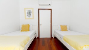 A room with two single beds, a door, an air conditioning unit, and a framed artwork on the wall.