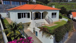 Ein zweistöckiges Haus mit rotem Ziegeldach, einem Balkon und einem kleinen Garten mit rosa Blumen.