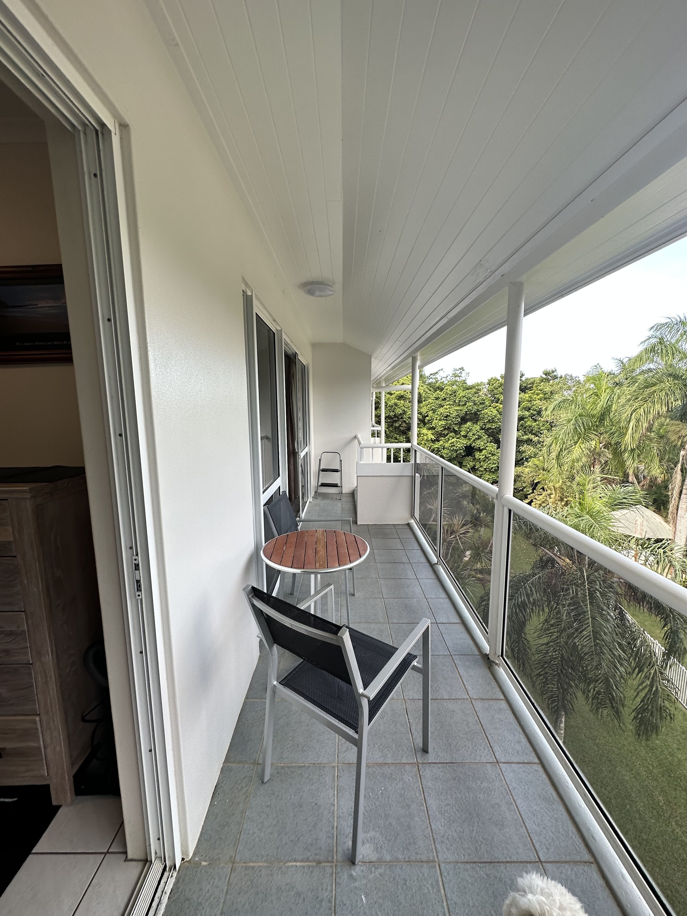 A balcony with a table and chairs, a view of greenery, and a white railing.