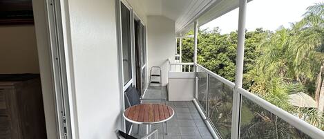 A balcony with a table and chairs, a view of greenery, and a white railing.