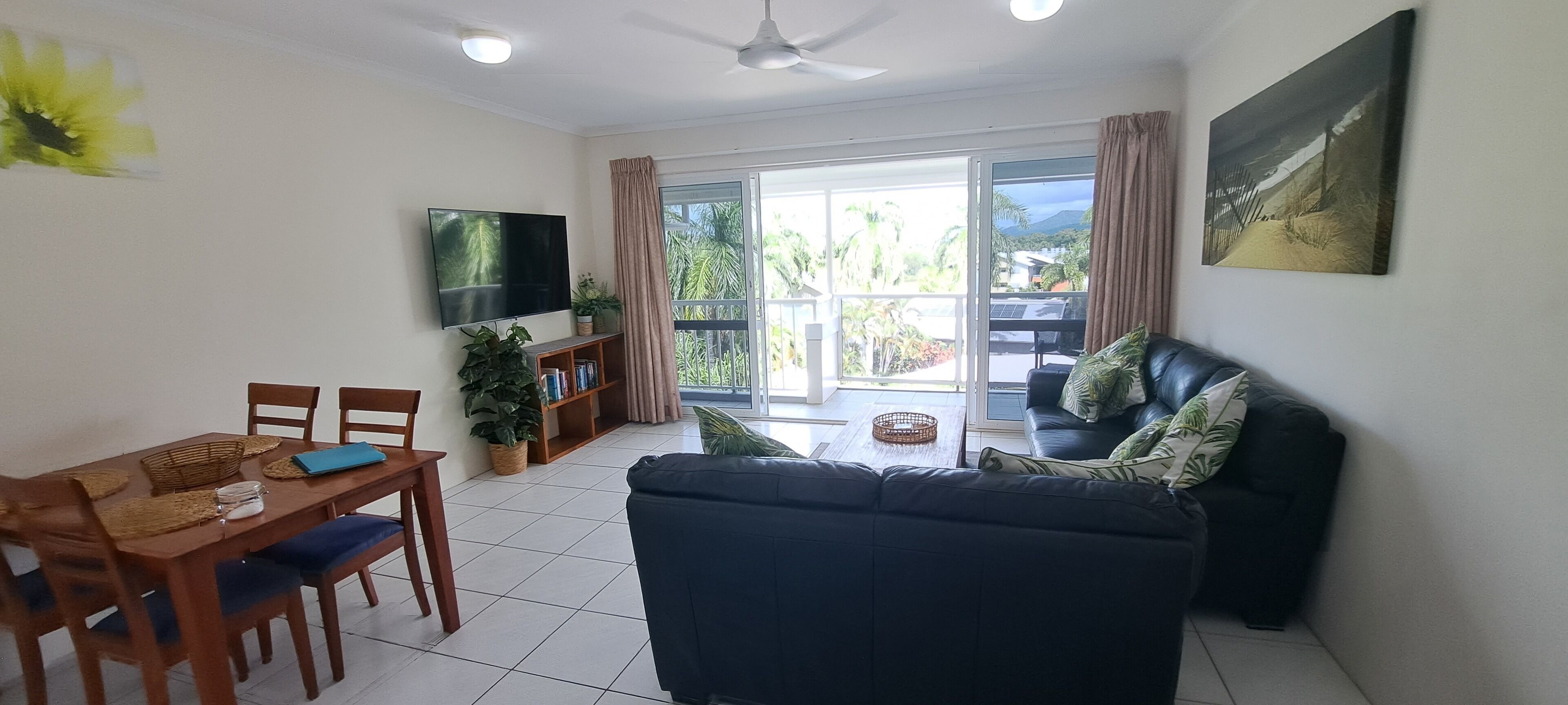 A living room with a sofa, TV, dining table, chairs, and a balcony with a view.