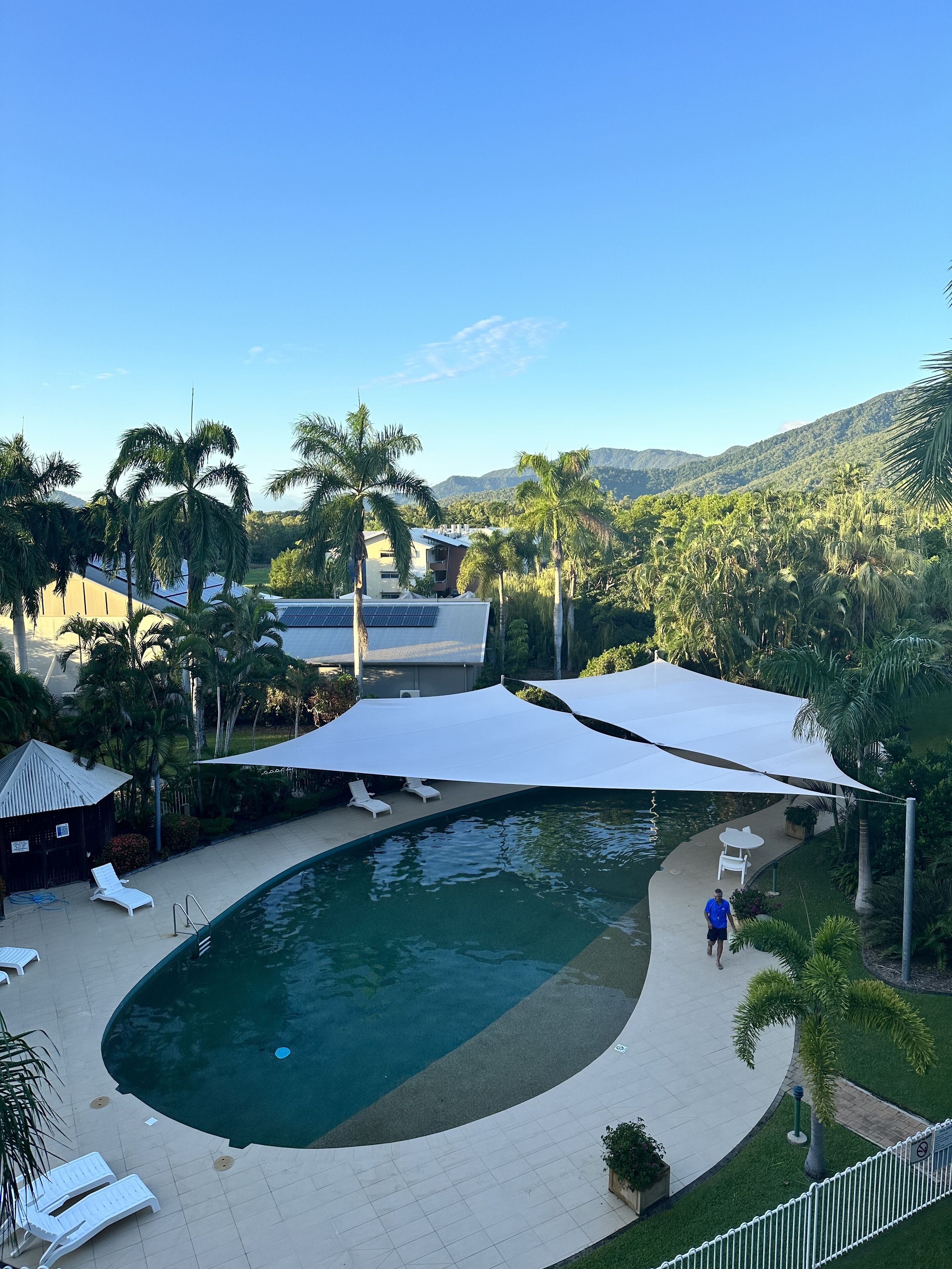 A swimming pool with sun loungers and a white canopy, surrounded by palm trees and a view of mountains.
