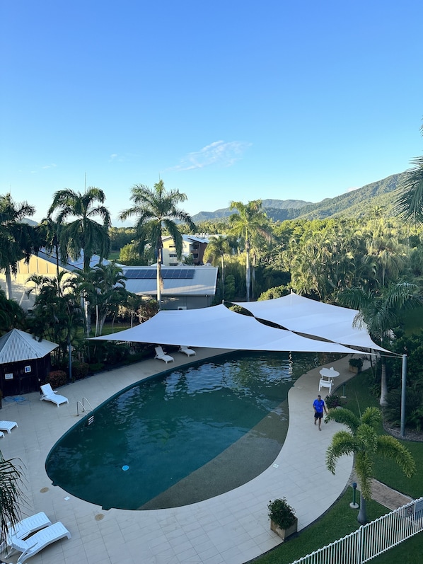 A swimming pool with sun loungers and a white canopy, surrounded by palm trees and a view of mountains. - Palm Cove Coral coast resort apartment got the lot Tropical Views Wi-Fi Netflix (Palm Cove)