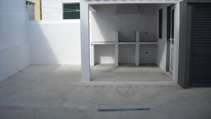 A covered outdoor area with a concrete floor, a metal vent, and a white wall with a window.