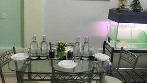 A dining area with a glass table surrounded by chairs, a framed artwork on the wall, and a fish tank on the side. - Bukit Bentong Homestay (Bentong)