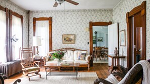 A traditional living room with a sofa, armchairs, a coffee table, and a fireplace. There is a dining area visible in the background. - 150 Year Old Home Situated in the Picturesque Rolling Hills of Southwest WI (Lone Rock)