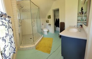 Ein Badezimmer mit Duschkabine aus Glas, Toilette, Waschbecken und einem gelben Teppichboden.