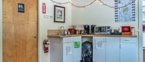 A kitchenette with a sink, coffee maker, microwave, and cabinets. There is a fire extinguisher, a framed picture, and a map on the wall.