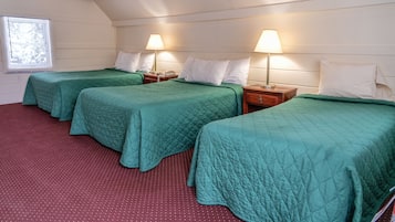A room with three single beds, each with a green quilt and white pillows, wooden headboards, and bedside lamps.