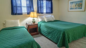 A room with two beds, each with a green bedspread, a nightstand with a lamp, and a painting on the wall.