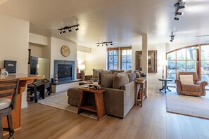 Amplia sala de estar con chimenea, un conjunto de sofás, un comedor con mesa y sillas, y grandes ventanales con vistas al exterior.