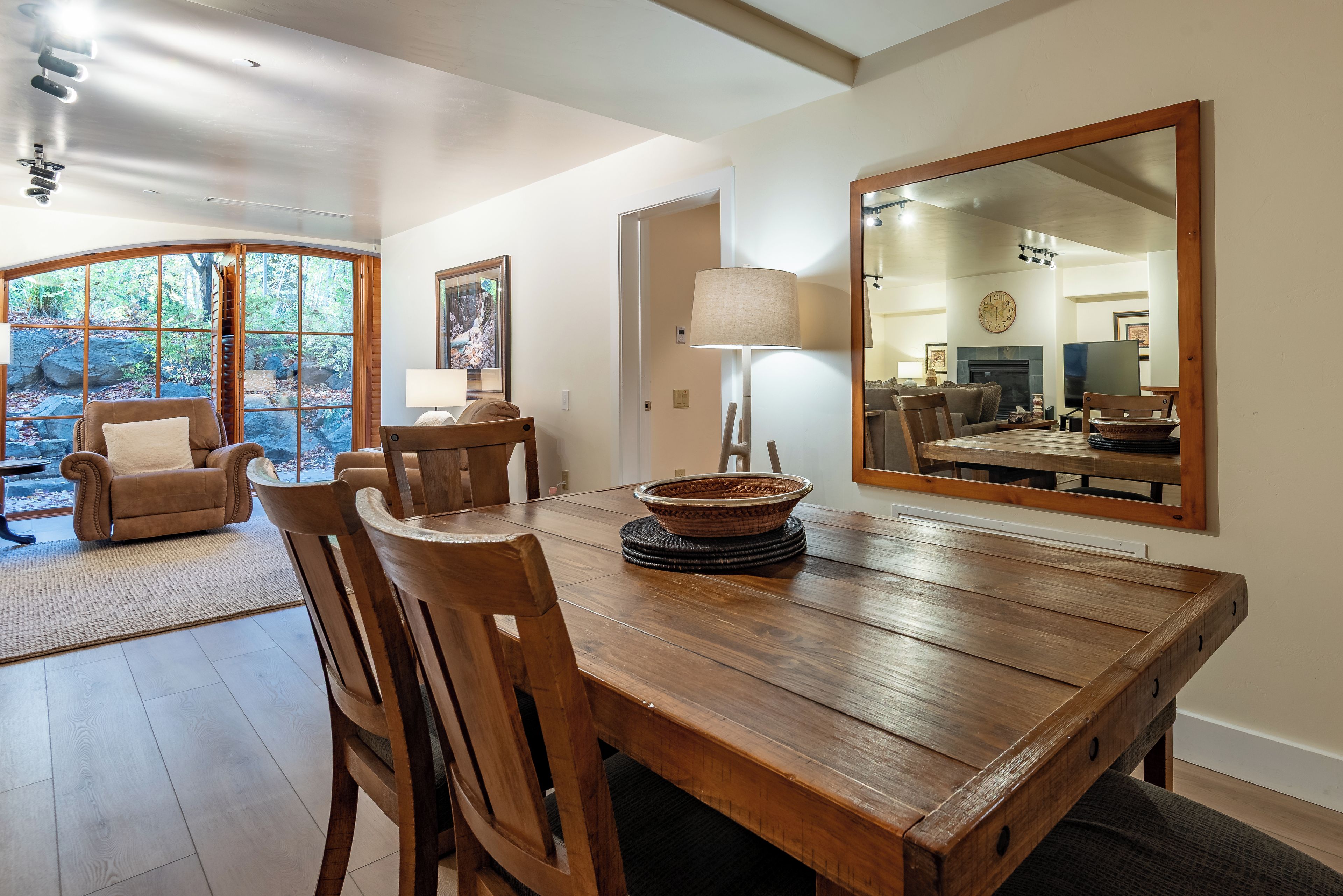 Un coin repas avec une table en bois, des chaises, une lampe et un grand miroir.