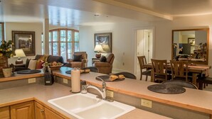 A spacious kitchen with a large island, wooden cabinets, and a dining area with a table and chairs. - Thunder Springs Condo A26 - Cozy Condo w/ Access to Zenergy Pool & Garage (Ketchum)
