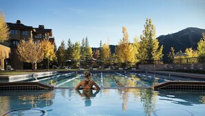 A swimming pool with a person in the water, surrounded by trees and buildings. - Thunder Springs Condo A26 - Cozy Condo w/ Access to Zenergy Pool & Garage (Ketchum)