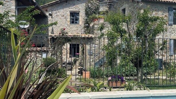 Un edificio de piedra con piscina, rodeado de vegetación y montañas.