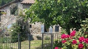 Un edificio de piedra con tejado de tejas, un patio cubierto de césped, una verja metálica y flores rosadas.