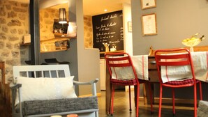 Un café acogedor con una pared de piedra, un banco de madera, dos sillas rojas y una pequeña mesa con una taza y un libro.