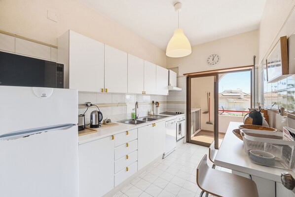A modern kitchen with white cabinets, a built-in oven, and a large window.