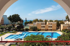 A swimming pool with a view of the sea, surrounded by greenery and buildings.
