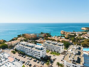 A coastal hotel with multiple buildings, a parking lot, and a view of the sea.