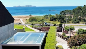 A coastal view with a beach, a mountain in the distance, and a modern building with a glass roof. - BEACH FRONT, SPA, SWIMMING POOLS, TENNIS, PADDLE, LARGE GARDEN, PLAYGROUND, CHILDREN'S PLAYGROUND, PLAYGROUND, TENNIS COURTS, PADDLE, LARGE GARDEN, CHILDREN'S PLAYGROUND, CHILDREN'S PLAYGROUND, CHILDREN'S PLAYGROUND. (O Grove)