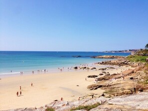 Una spiaggia con acqua cristallina, una battigia sabbiosa e un terreno roccioso.