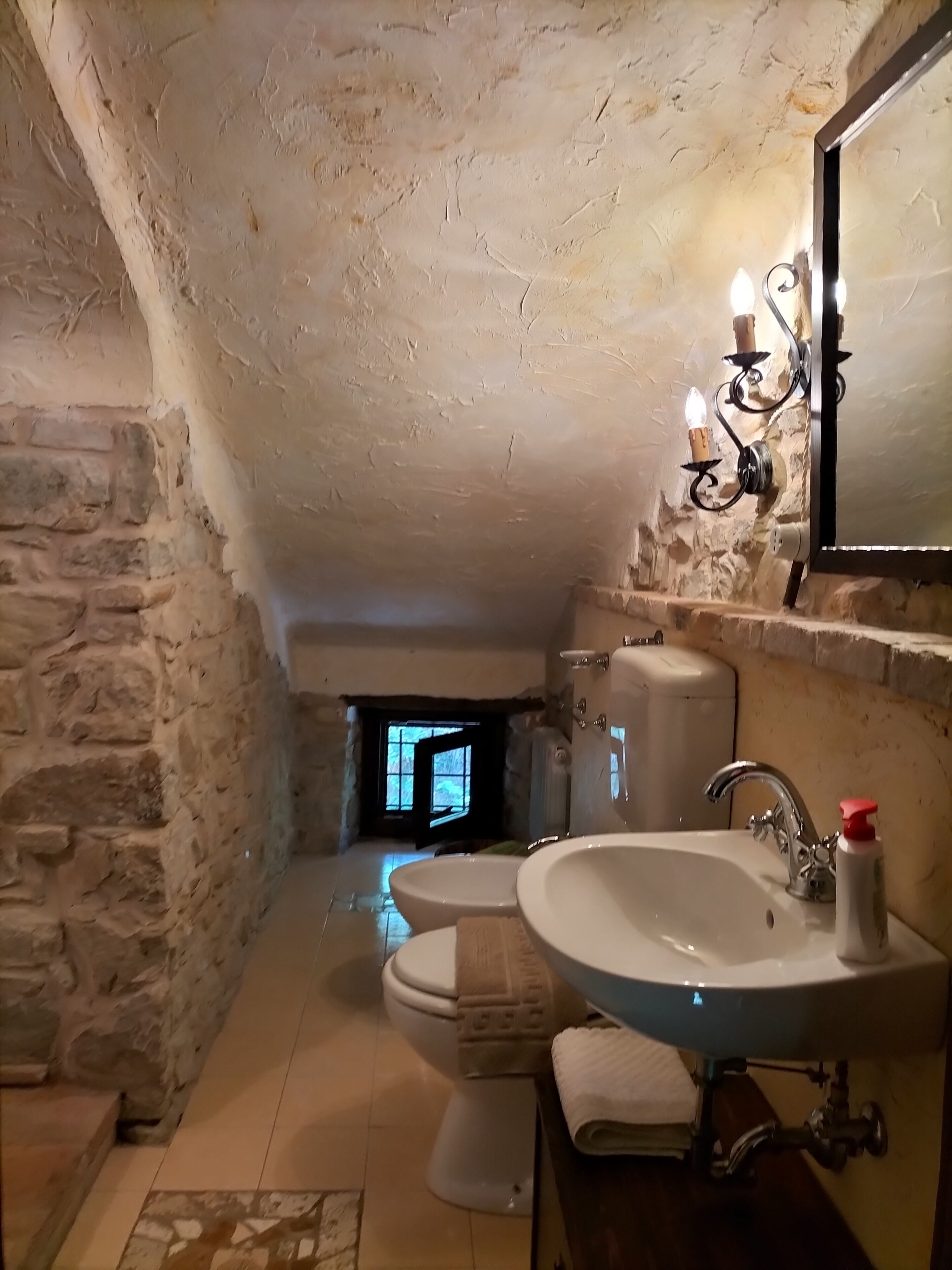 A rustic bathroom with a stone wall, a white sink, a toilet, and a shower.
