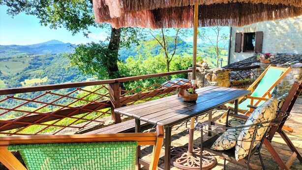 A wooden deck with a table and chairs overlooking a mountainous landscape. - Stone Casale Apartment with Pool & Terrace: Sibillini to Sea View (Penna San Giovanni)
