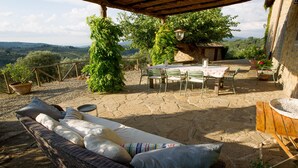 Un patio exterior con un sofá de mimbre, una mesa lista para comer y vistas al campo.
