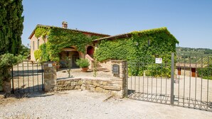 Una casa de piedra con techo de tejas rojas, cubierta parcialmente por hiedra verde, y una entrada con puerta de hierro forjado.