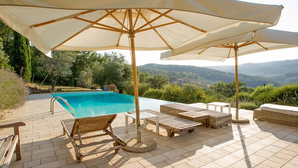 Zona de piscina con vistas al campo, sillones de madera y sombrillas.