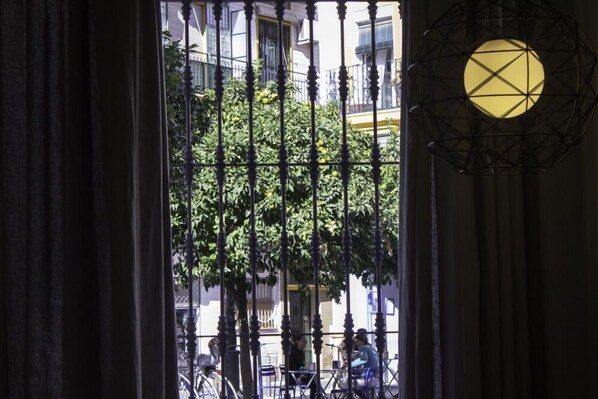 A view through a window with iron bars, a tree, and a building with balconies in the background. - APT. IN SEVILLA CENTER. NEW, ORIGINAL LOFT. CHARMING. WIFI. 2 BEDROOMS (Sevilla)