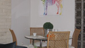 Un salon moderne comprenant un canapé, une table basse en verre, des fauteuils en osier, une table à manger avec des chaises, une plante en pot et une fresque murale représentant des zèbres.
