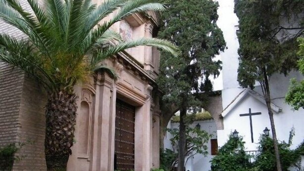 Une cour intérieure avec un bâtiment doté d’une grande porte en bois et de colonnes, entourée de plantes en pot et d’arbres.