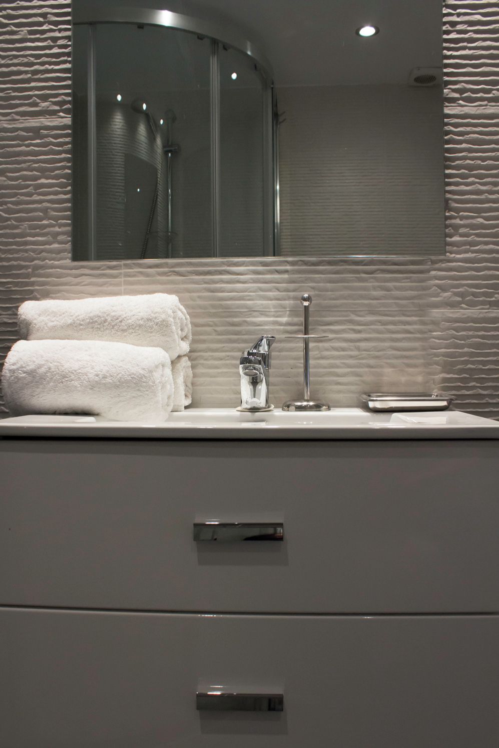 A bathroom with a modern design, featuring a large mirror, a towel rack with folded towels, a glass of water, and a sink.