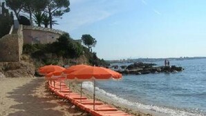 A beach with orange umbrellas and a stone wall. - Luxury building with swimming pool and sea access (Vallauris)