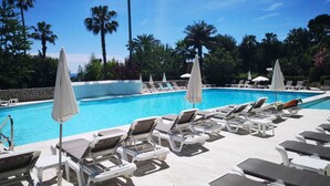 A poolside area with lounge chairs and umbrellas, surrounded by palm trees. - Luxury building with swimming pool and sea access (Vallauris)