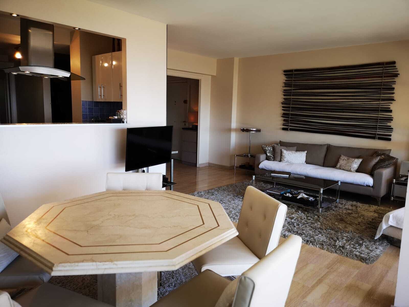 Un salon moderne avec une grande table octogonale, un canapé et un téléviseur.